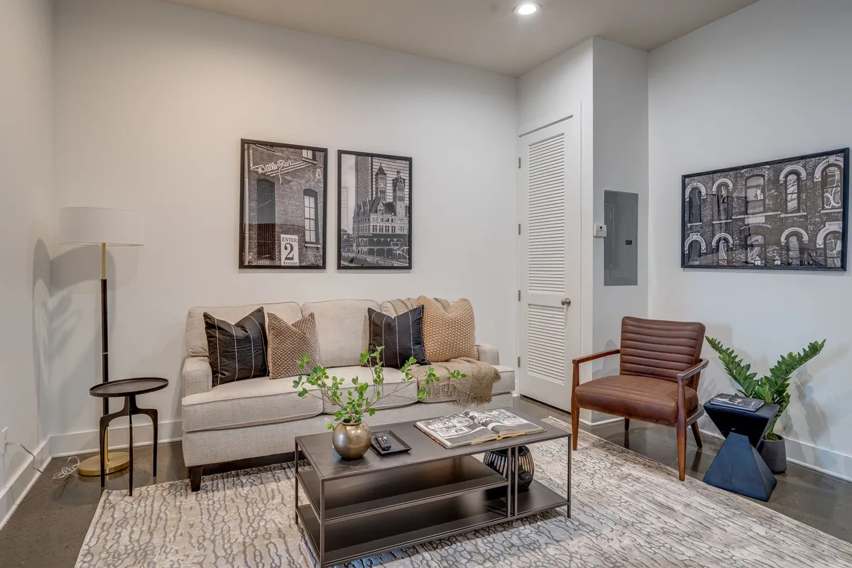 A stylish and comfortable living room featuring a cozy sofa, elegant coffee table, eye-catching artwork on the wall, a warm floor lamp, and an inviting armchair. The space is arranged for both relaxation and social gatherings, with a layout ideal for conversation or movie nights.