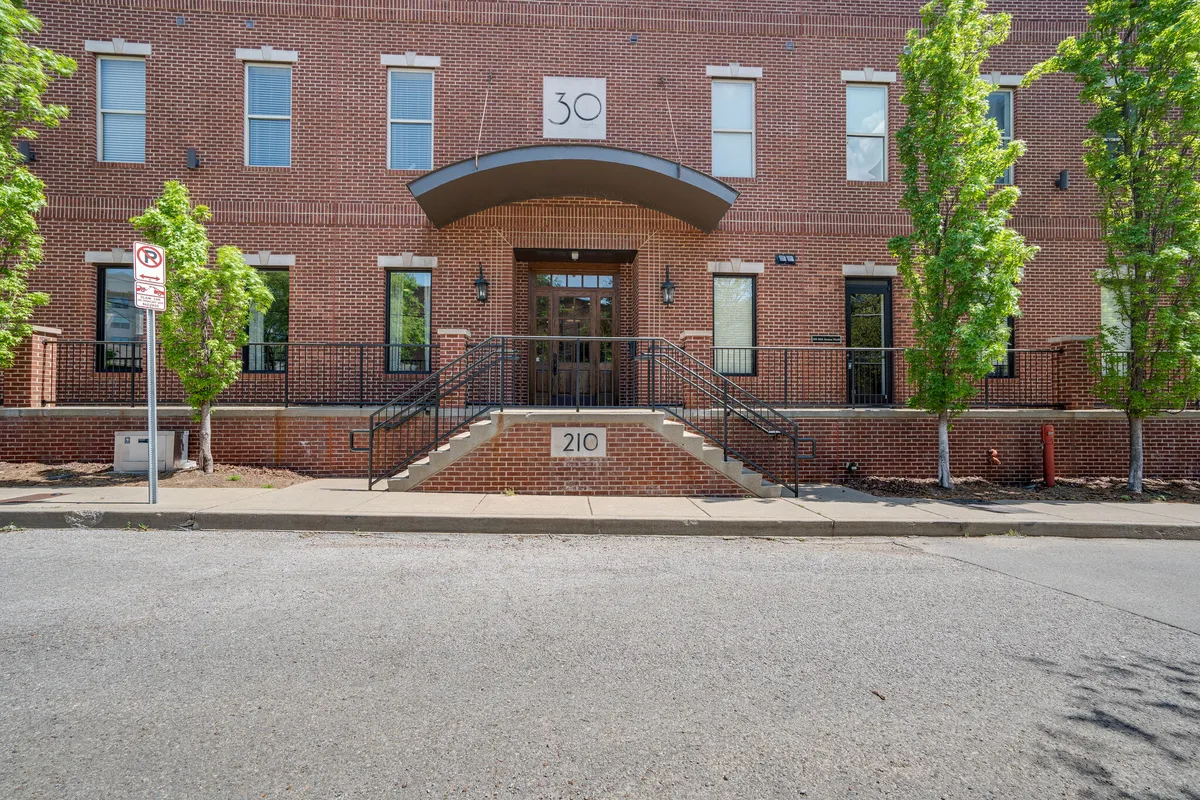 A welcoming exterior shot of the building's entrance, featuring entrance steps, the modern facade, number signage, and landscaped trees. The image conveys a sense of arrival and highlights the building's professional appearance and accessibility.