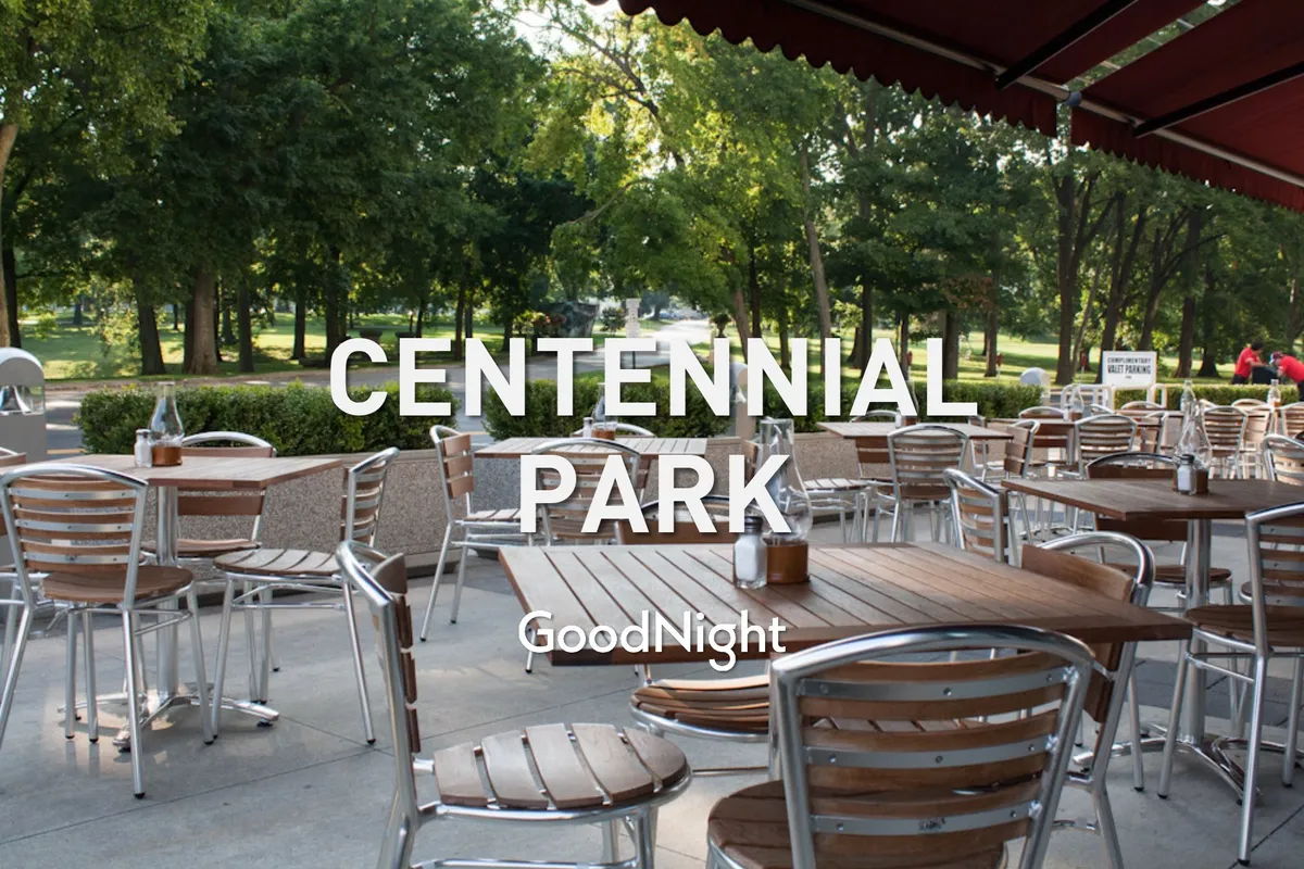 This image features outdoor wooden tables and metal chairs nestled amid lush greenery, all shaded by a canopy awning. The scene suggests a casual, sociable atmosphere perfect for group picnics, relaxing with friends, or enjoying nature close to home.