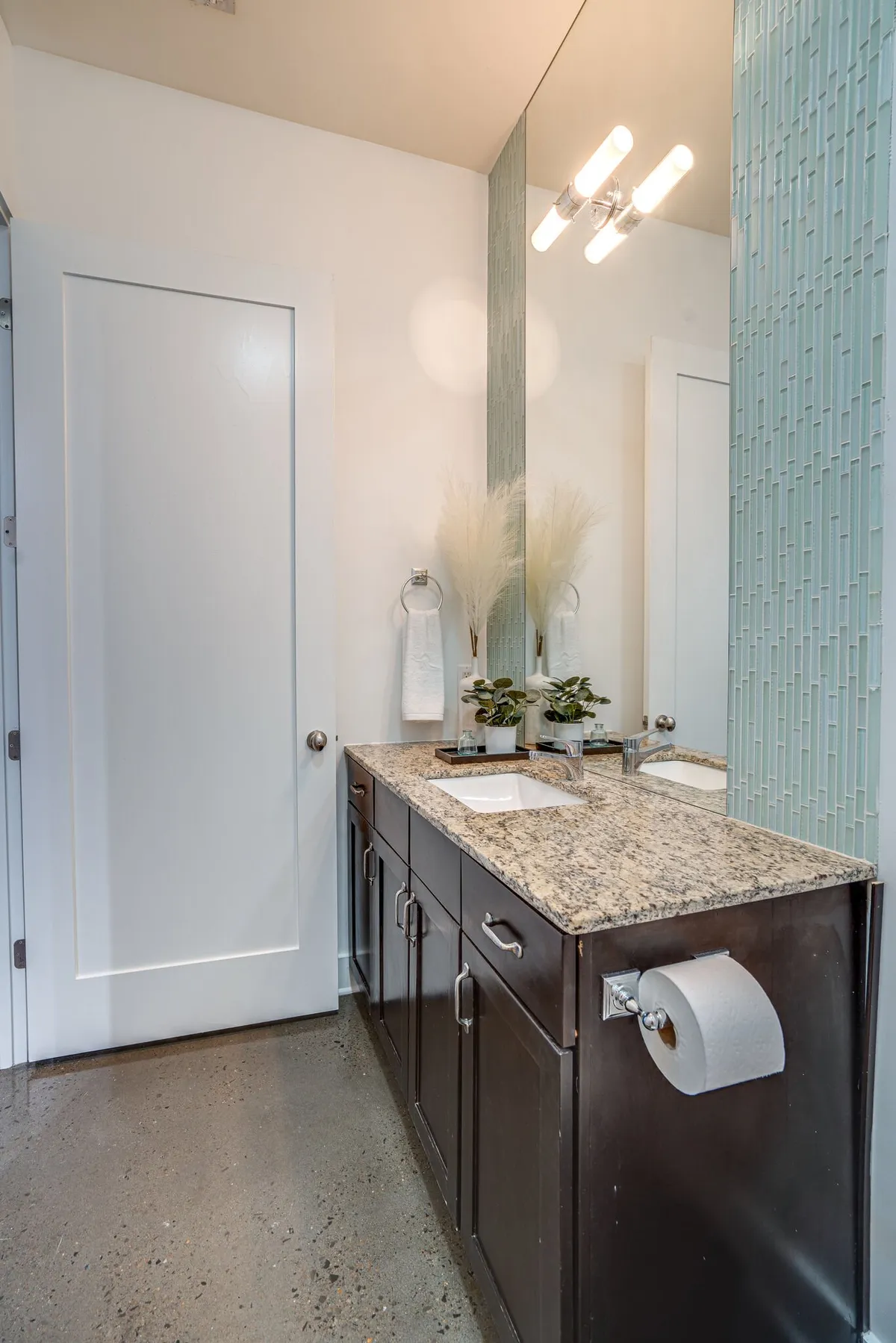 A sleek, modern bathroom with a granite countertop, contemporary sink, a stylish mirror, and decorative green plants. Morning light streams in, creating a spa-like, serene setting ideal for self-care routines.