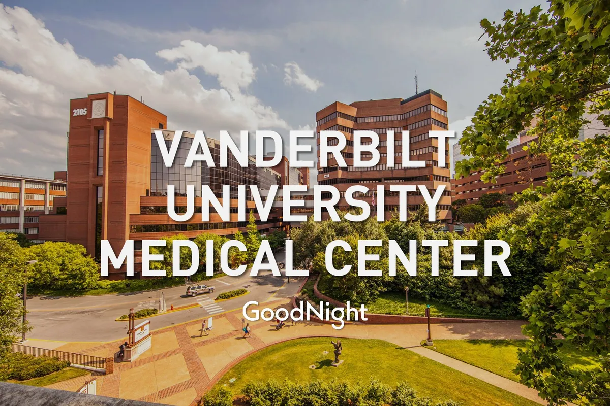 An exterior shot of the Vanderbilt University Medical Center building, surrounded by landscaped gardens and pathways with people walking. The scene is calm and reassuring, emphasizing green spaces and walkable outdoor environments.