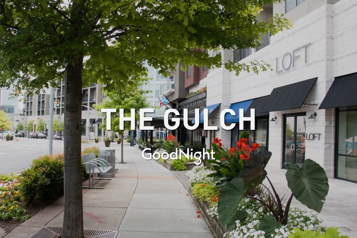 A cheerful outdoor shopping and dining district, complete with flower beds, inviting benches, and vibrant storefronts. Visitors can be seen strolling, shopping, or relaxing, suggesting an atmosphere perfect for discovering new flavors and local gems.